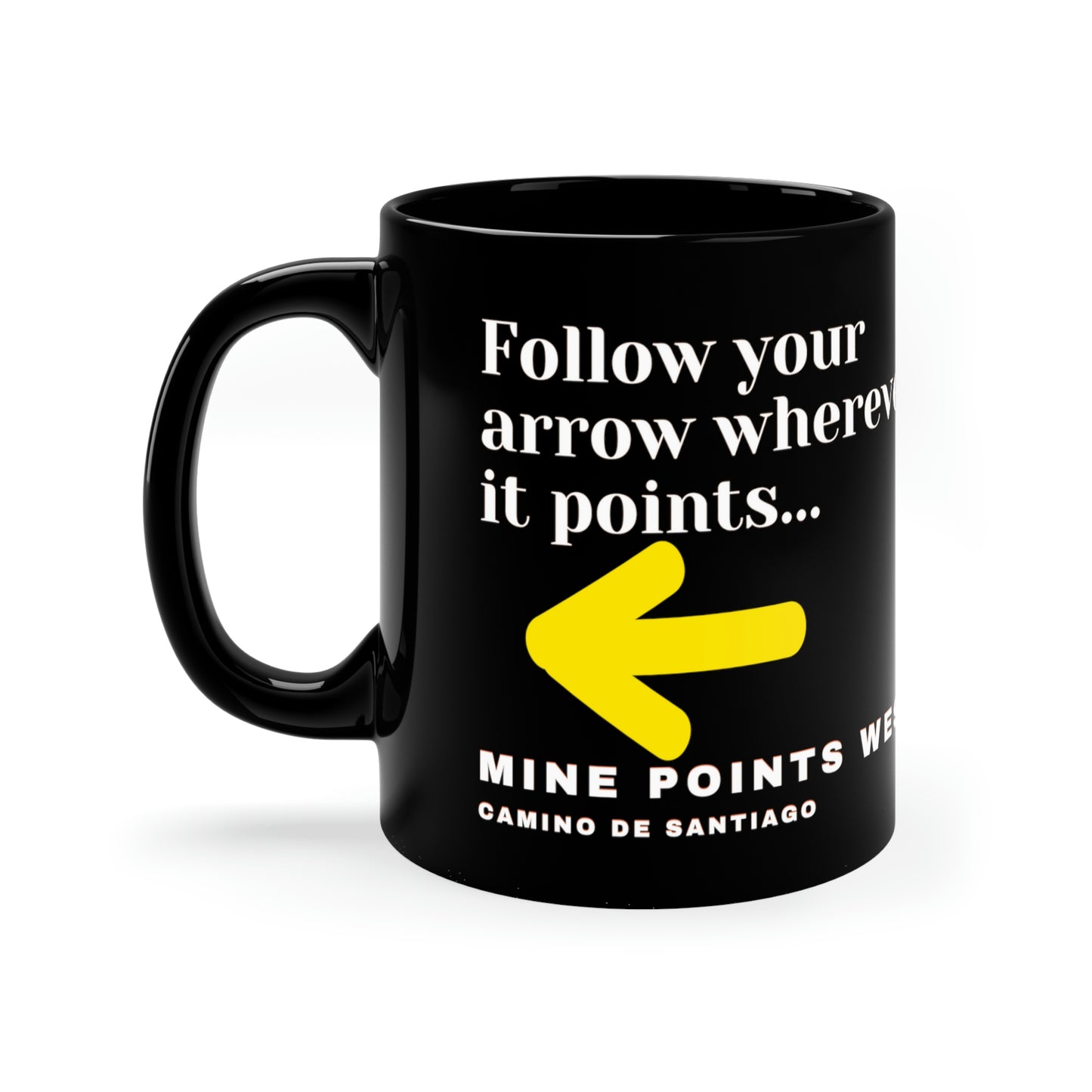 Camino Frances - This black ceramic mug has a slogan in white letters that says, Follow your arrow wherever it points . . . With a yellow arrow below it then below that the words, Mine Points West and under that Camino de Santiago. The Mug is surrounded by white background.