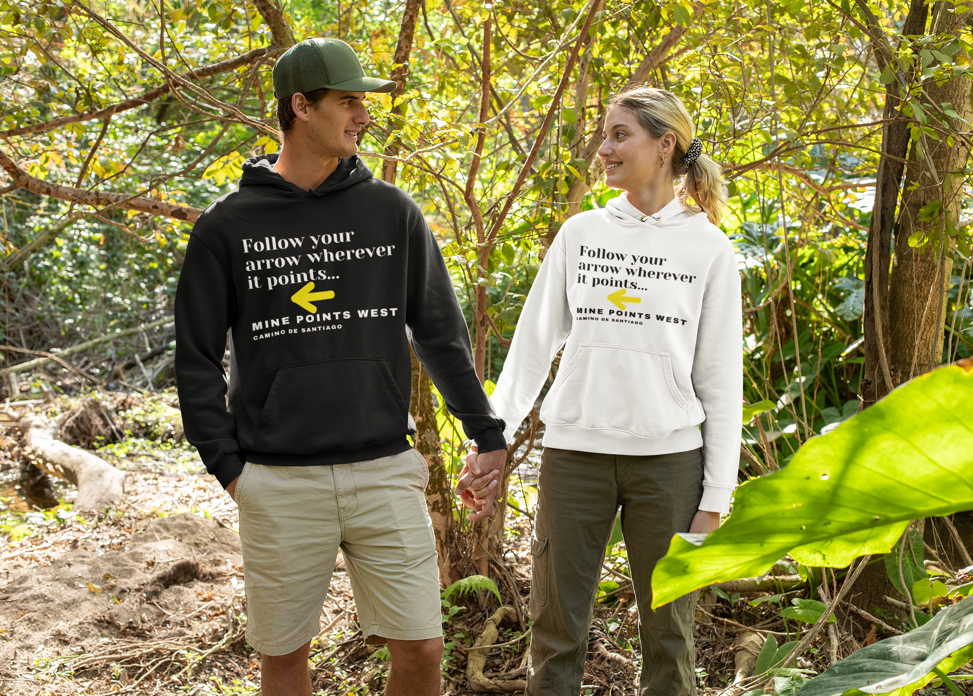 Camino Frances hiking hoodie worn by a couple hiking in the woods. The male is wearing the black hoodie and the female on the right is wearing the white hoodie.